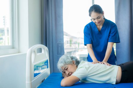 Foto de Una joven enfermera asiática en un asilo cuida de una mujer mayor. El médico que atiende proporciona servicios de fisioterapia para que los pacientes de edad avanzada hagan ejercicio para su salud. - Imagen libre de derechos
