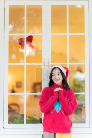 Photo for Young Asian woman in Santa hat smiling and holding Christmas gifts smile happily While decorating the Christmas tree at home, the idea of celebrating New Year's Day - Royalty Free Image
