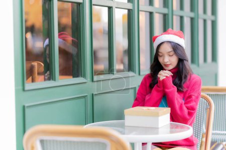 Foto de Mujer asiática joven en el sombrero de Santa sonriendo y sosteniendo los regalos de Navidad sonrisa felizmente Al decorar el árbol de Navidad en casa, la idea de celebrar el Día de Año Nuevo - Imagen libre de derechos