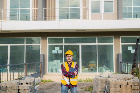 Photo for Young Asian civil engineer or construction supervisor wearing a helmet looks away and smiles while inspecting a construction site. - Royalty Free Image