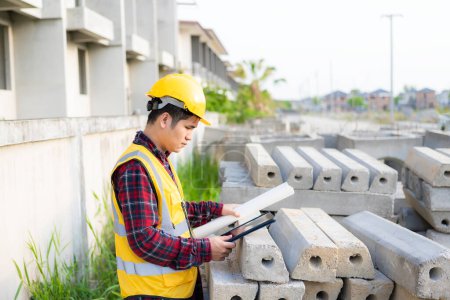 Téléchargez les photos : Jeune ingénieur civil asiatique ou superviseur de la construction portant un casque regarde loin et sourit lors de l'inspection d'un chantier de construction. - en image libre de droit