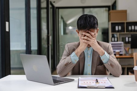 Photo for Tired Millennial businessman sitting at laptop touching head feeling tired overworked Suffering from weak eyesight, headache, office syndrome concept. - Royalty Free Image