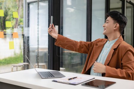 Téléchargez les photos : Jeune homme d'affaires asiatique en costume décontracté utilise un ordinateur portable et parle au téléphone pour communiquer avec les clients. réunion en ligne d'affaires en ligne - en image libre de droit
