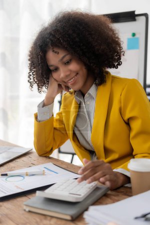 Téléchargez les photos : La jeune femme noire qui travaille avec des documents financiers à la maison doit utiliser une calculatrice avant de payer un reçu d'impôt en ligne. Planifiez votre budget pour économiser. image verticale - en image libre de droit