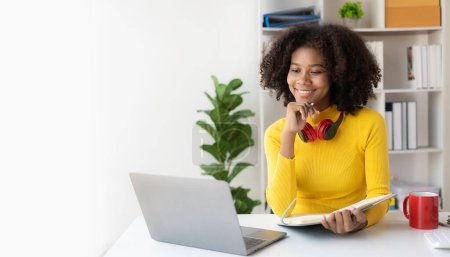 Foto de Chica afroamericana en auriculares viendo video lección en la computadora en la sala de estar en casa, feliz en los auriculares que tienen clase en línea utilizando el ordenador portátil - Imagen libre de derechos