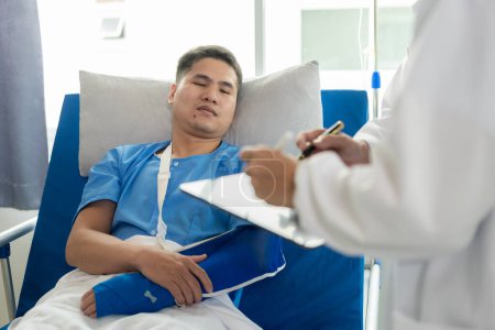 Photo for An Asian male patient lies in a hospital bed and is carefully looked after by a doctor. Doctor giving advice to male patient Working on health disease diagnosis - Royalty Free Image