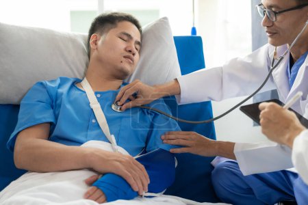 Foto de Un paciente masculino asiático yace en una cama de hospital y es cuidadosamente atendido por un médico. Médico dando consejos al paciente masculino Trabajando en el diagnóstico de enfermedades de salud - Imagen libre de derechos
