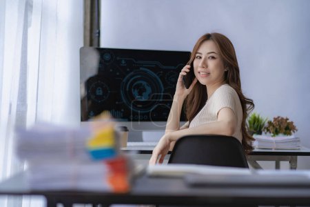 Photo for Asian businesswoman smiling happily using smartphone sitting at table in office Female financial accounting company employee with growth statistics charts and graphs at home office. - Royalty Free Image