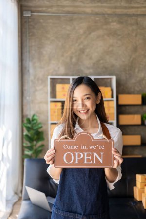 Photo for Happy young business owner standing holding open sign Happy Asian woman wearing an apron hanging a shop opening sign smile happily Proud in personal business - Royalty Free Image