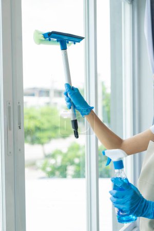 Photo for Maid wearing an apron provides cleaning services at home. Close-up of a young woman cleaning a new house or apartment while moving in copy space - Royalty Free Image