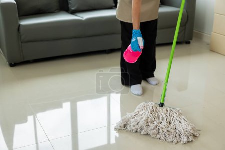 Photo for Maid wearing an apron provides cleaning services at home. Close-up of a young woman cleaning a new house or apartment while moving in copy space - Royalty Free Image