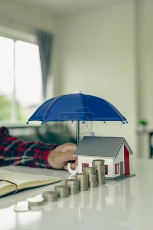Téléchargez les photos : Parapluie bleu couvrant un modèle de maison sur une table en bois Assurance de biens, concept d'assurance hypothécaire L'assurance est le contrôle des risques dans l'entreprise immobilière. - en image libre de droit