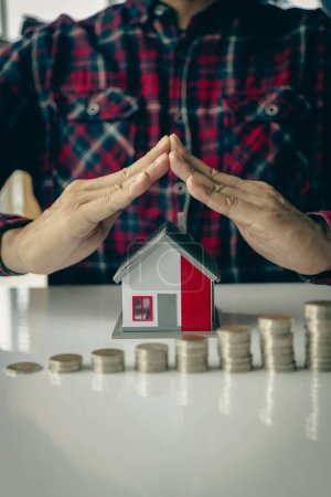 Photo for Protecting the house with house hands in charge of a man showing a gesture to protect a wooden house model. Housing. Home protection and insurance against natural disasters and theft. Close-up. - Royalty Free Image
