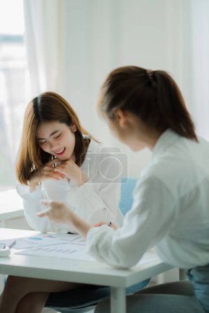 Photo for Two Asian female accountants have team meeting to summarize financial information in business office, creative female executive using tablet PC and smiling - Royalty Free Image