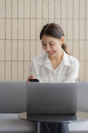 Photo for Asian woman working using a laptop at home or in a coffee shop is sitting at a table typing using a computer. online business ideas - Royalty Free Image