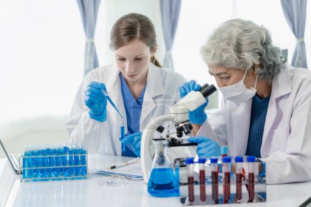 Téléchargez les photos : Deux belles jeunes scientifiques et femmes âgées travaillent dans un laboratoire avec des éprouvettes et font des recherches avec des éprouvettes faisant des recherches sur les produits chimiques bleus dans l'industrie de la santé. - en image libre de droit