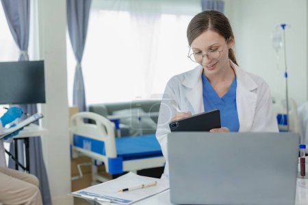 Téléchargez les photos : Portrait d'une belle jeune femme médecin assise à une table Travail dans une clinique médicale, dans le bureau d'un résident à un ordinateur - en image libre de droit