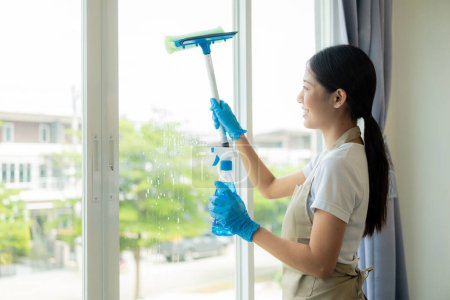 Photo for Beautiful Asian housewife doing housework and cleaning the house with an apron, using a vacuum cleaner, mop, cloth to clean the floor in the living room. Happy housewife doing housework - Royalty Free Image