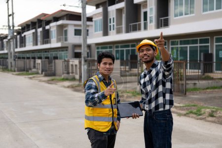 Photo for Two young Asian engineers, architects, men are talking about construction. Follow the project to create a tabletop industrial plan at an outdoor site. - Royalty Free Image