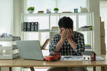 Photo for A young Asian man is stressed about bills, car payments, house payments, and holds his head in his hands as he looks at the bills. Confused about financial information or worried about spending money - Royalty Free Image
