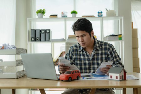 Téléchargez les photos : Jeune homme asiatique calcule les paiements de voiture Versements à la maison dans la planification financière et le revenu concepts d'approbation d'actifs, l'achat de voitures et de maisons, check-list, prêts à domicile, taxes à la maison - en image libre de droit