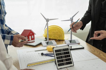 Photo for Construction crews begin new project plans to discuss a renewable energy construction project that includes wind turbines and solar cells. and the house on the table in the close-up - Royalty Free Image