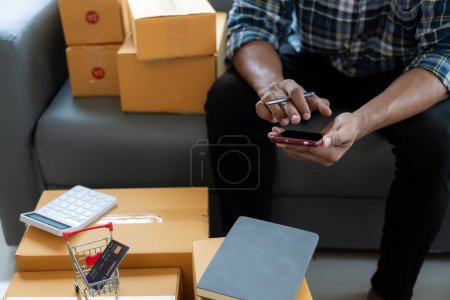 Photo for Small business entrepreneur, SME, independent man, working from home. Use smartphones and laptops for commercial inspection, online marketing, packaging boxes, SME sellers, concepts, close-up shots. - Royalty Free Image
