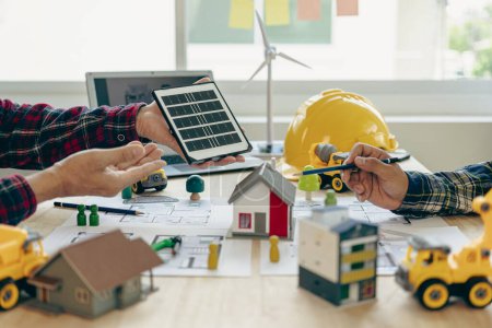 Photo for Construction crews begin new project plans to discuss a renewable energy construction project that includes wind turbines and solar cells. and the house on the table in the close-up - Royalty Free Image