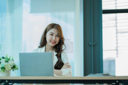 Photo for Cheerful Asian woman working with laptop in office, happy in formal suit working in office Charming smiling female office worker, financial accounting concept - Royalty Free Image