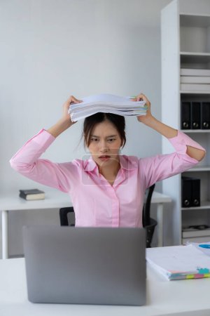 Téléchargez les photos : Jeune femme asiatique met ses mains sur sa tête se sentant fatigué, irrité et stressé par le travail acharné au bureau et insatisfait de son travail tout en regardant les documents de rapport. - en image libre de droit