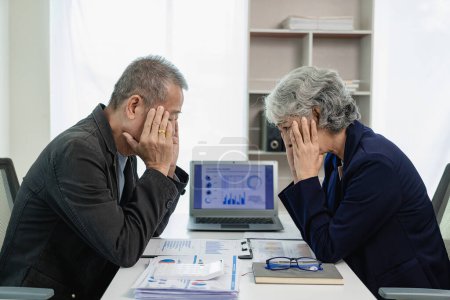 Foto de Dos hombres de negocios asiáticos mayores, hombres y mujeres, están estresados con el papeleo y están cansados, tienen dolores de cabeza y síndrome de oficina de trabajar duro con documentos financieros en el escritorio de la oficina. - Imagen libre de derechos