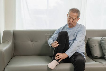 Photo for Old Asian man with knee and leg joint pain on the sofa pain in the elderly Caring for the health of the elderly - Royalty Free Image