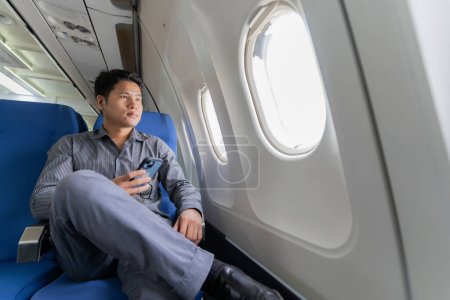 Photo for Young professional Asian man working with laptop computer and smartphone while sitting in airplane in airplane cabin during business and leisure travel. - Royalty Free Image