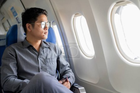 Photo for Young professional Asian man working with laptop computer and smartphone while sitting in airplane in airplane cabin during business and leisure travel. - Royalty Free Image