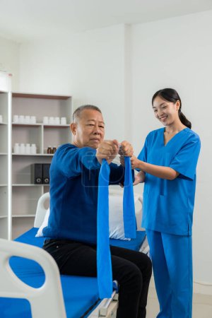 Photo for An old Asian man is doing physical therapy with the support of a nurse in the living room by exercising for a patient with his caregiver in nursing care. Physical therapy for the elderly - Royalty Free Image