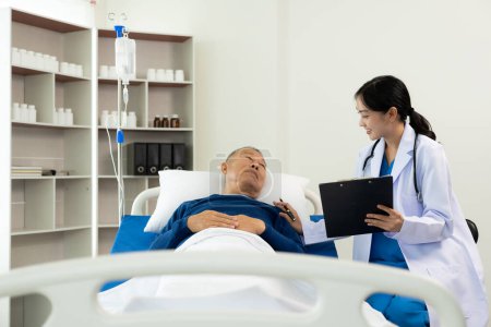 Foto de Un anciano hospitalizado yace en la cama mientras un médico le revisa el pulso. Médico o enfermero examinando a un paciente masculino mayor, cuidándolo y animándolo en la habitación del hospital, acostado en la cama. - Imagen libre de derechos