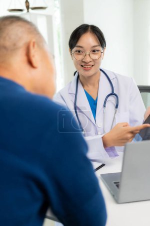 Téléchargez les photos : Asiatique professionnel femme médecin parler avec patient masculin sur sa douleur et les symptômes tout en donnant consultation à table dans la salle d'examen à l'hôpital de soins de santé - en image libre de droit
