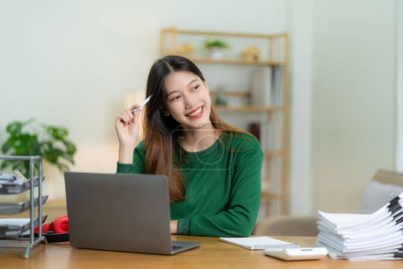 Foto de Chica asiática ambiciosa que trabaja desde casa Mirando la pantalla del ordenador portátil y sonriendo, comprobando el correo o haciendo investigación mientras trabaja de forma remota, negocio de startups en línea, telemarketing - Imagen libre de derechos