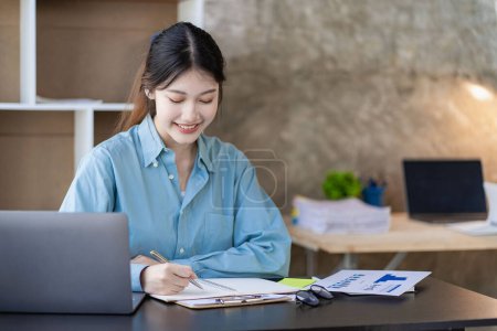 Téléchargez les photos : Professionnel asiatique femme comptable se concentre sur ses comptes de vente à l'aide d'une calculatrice et ordinateur portable à son bureau pour analyser les rapports et les documents d'affaires. - en image libre de droit