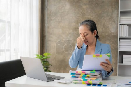 Photo for Stressed senior businesswoman feeling irritated and tired from heavy paperwork, tired, stressed out with a headache at work with laptop. Bookkeeping. Feeling migraine from overwork. - Royalty Free Image