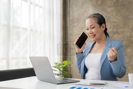 Téléchargez les photos : Femme d'affaires asiatique senior parlant au téléphone avec un client au bureau en prenant des commandes via un formulaire sur un site Web, concept d'entreprise financière - en image libre de droit