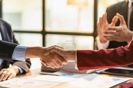 Photo for Businessman shaking hands with clients in conference room, team leaders meet with group to greet each other, handshaking showing trust and respect on table with documents Graph and laptop. Close up. - Royalty Free Image