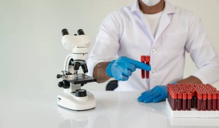Foto de El médico del hospital sostiene la prueba de vasos sanguíneos en el laboratorio con la muestra de sangre del estante con el analizador en el laboratorio - Imagen libre de derechos