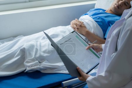 Foto de Paciente masculino de ascendencia asiática en cama recibe buenas noticias del médico sobre su recuperación en hospital, salud, concepto médico y de seguro. - Imagen libre de derechos