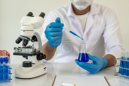 Foto de Científico asiático con máscara protectora para trabajar en un laboratorio, tubos de ensayo, microscopio en un laboratorio de química. desarrollo e investigación - Imagen libre de derechos