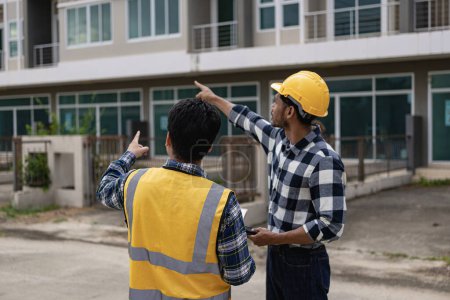 Photo for Contractor, male construction worker inspecting construction site, Asian engineer and young project managing partner working together in the workplace wearing safety helmets - Royalty Free Image