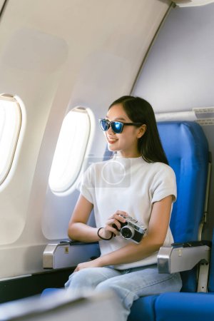 Foto de Joven mujer asiática viajero sentado cerca de la ventana y mirando por la ventana celebración de cuaderno en el avión, concepto de caminar - Imagen libre de derechos