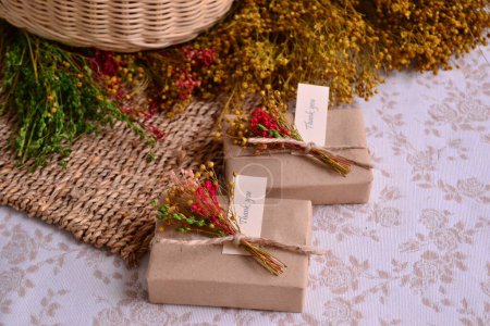 La decoración rústica de la boda favorece la caja de recuerdos artesanales en color marrón con flores y cinta de yute, jabón hecho a mano, fondo de mimbre