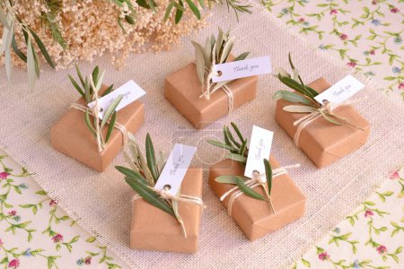 Wedding favors brown craft guest gifts box, handmade soap with olive leaves rustic decoration jute ribbon, mediterranean style ceremony decor, small gift, burlap and floral table cloth background