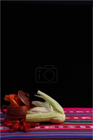 Photo for Products from the mountains of Peru. Corn, yellow chili, red chili on a tablecloth with the typical design pattern of the Inca sierra of Peru, Bolivia, Ecuador. With a black background - Royalty Free Image
